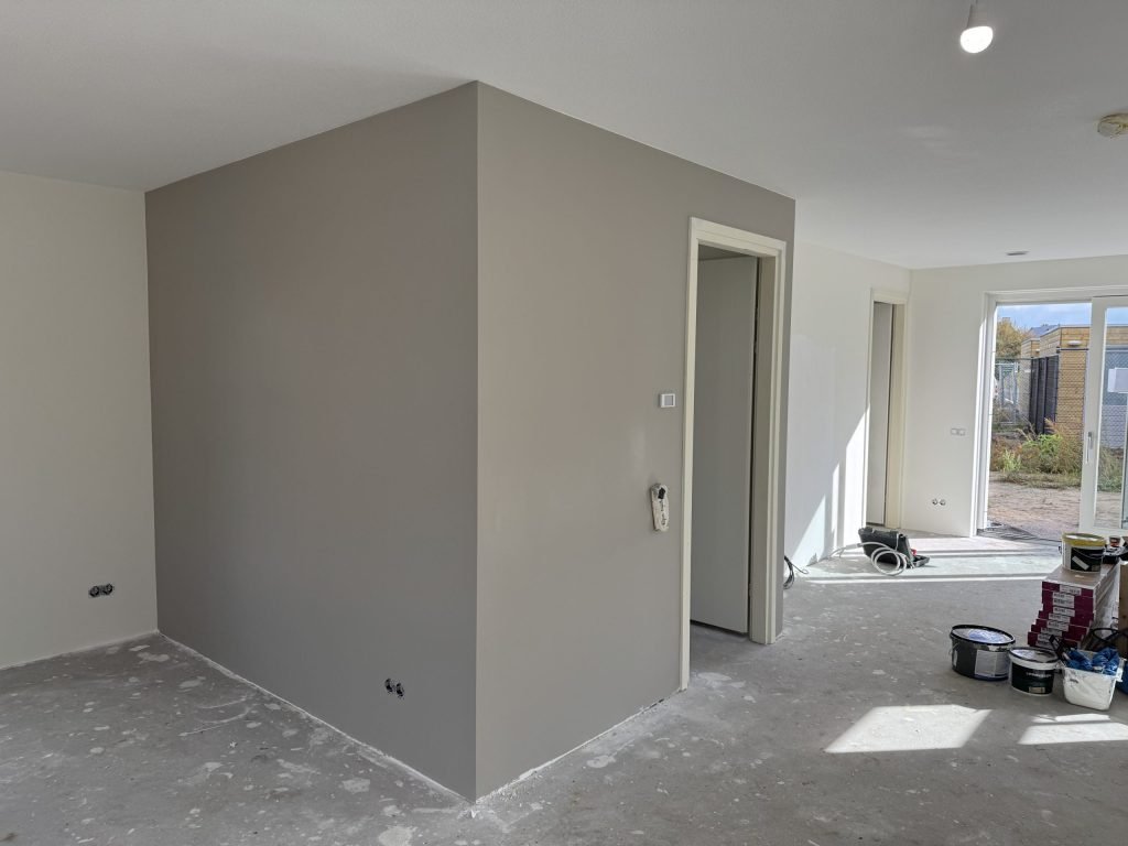 Nieuwbouwwoonkamer met een net gesausde grijze wand, emmers verf en een open tuindeur